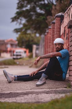 A young man sitting casually against a brick wall on a street in Kariega, South Africa.