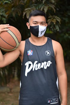 A young male basketball player wearing a mask and jersey outdoors.