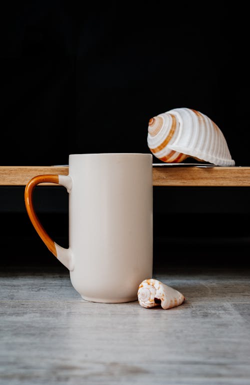 Cup of coffee on floor near shelf decorated with seashell