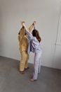 Woman in White Long Sleeve Shirt and White Pants Standing Beside White Wall