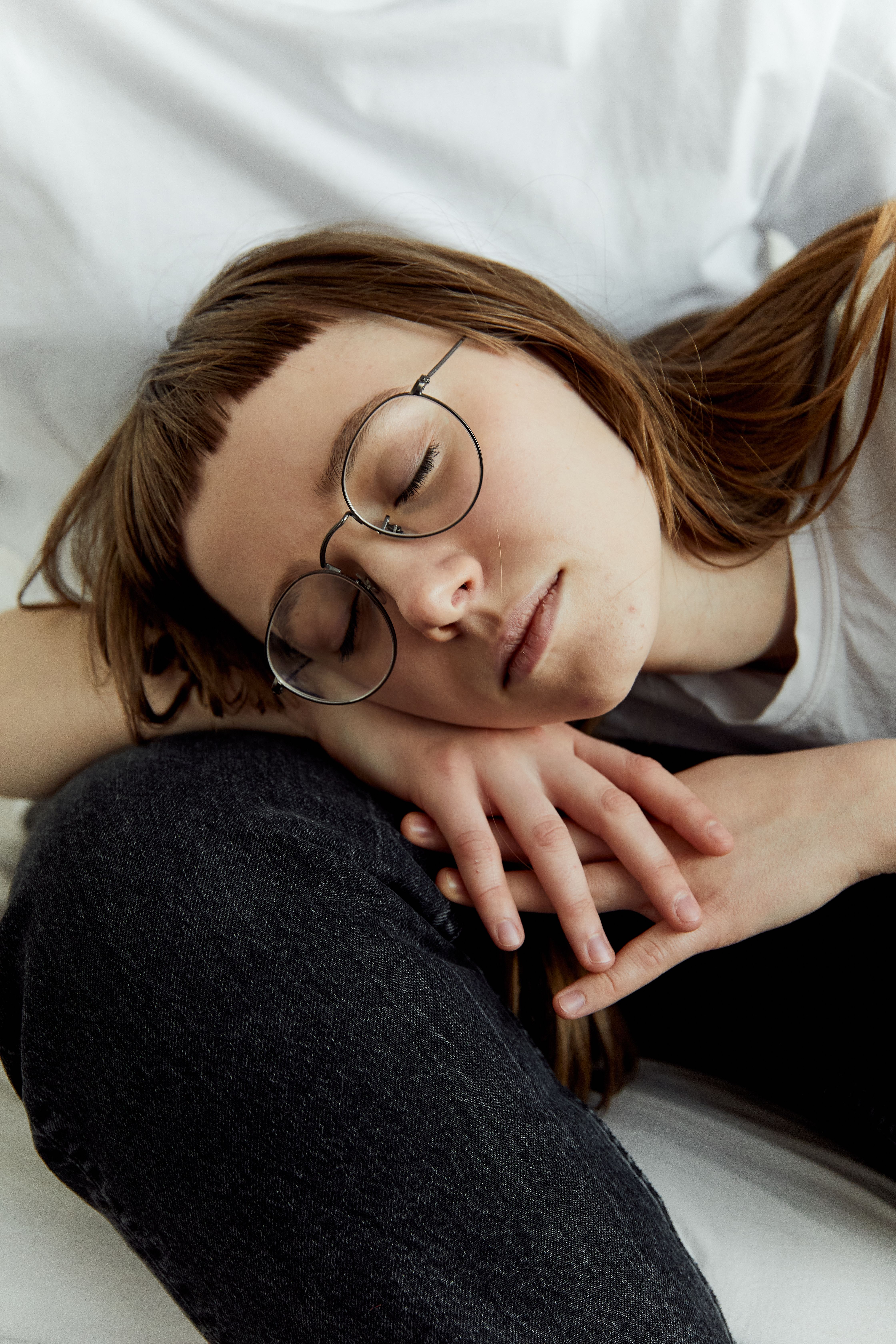 Young girl with glasses resting, eyes closed, in a serene indoor setting. Captured with artistry.