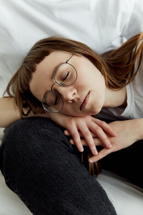 Free Young girl with glasses resting, eyes closed, in a serene indoor setting. Captured with artistry. Stock Photo