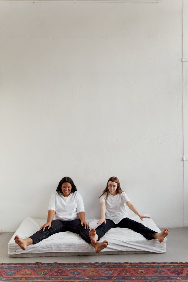 Two Women Sitting On A Mattress On The Floor