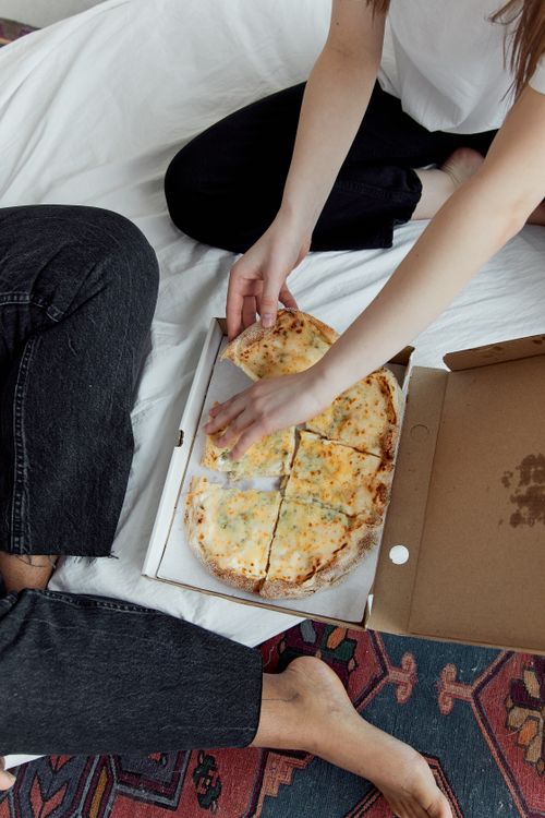 Free Two people enjoying a cheese pizza on a white blanket indoors, creating a cozy atmosphere. Stock Photo