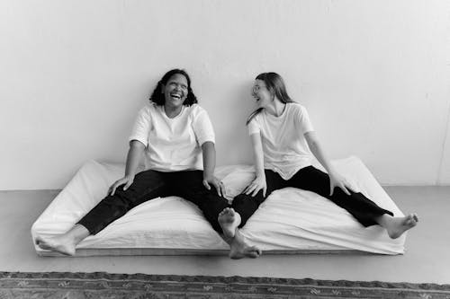 2 Women in White Tank Top and Black Pants Lying on Bed