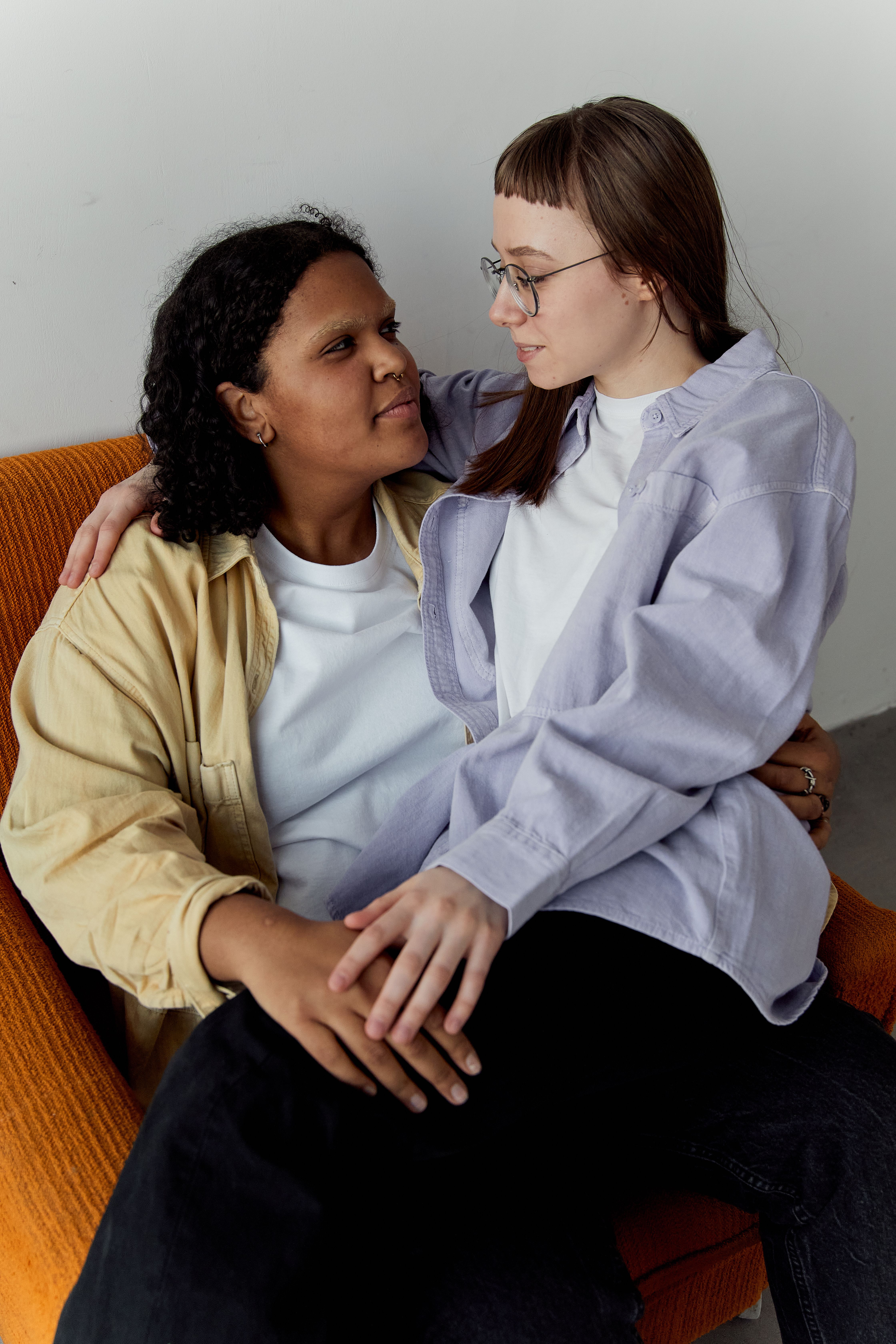 A loving couple enjoying a tender moment together while sitting on an orange chair in a cozy indoor setting.