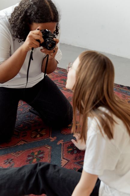 A photographer capturing an indoor session with a model sitting on a decorative carpet.
