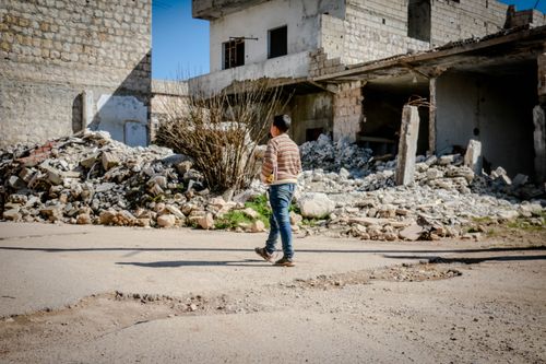 Free A young boy walking past rubble in a conflict-affected area of Idlib, Syria. Stock Photo
