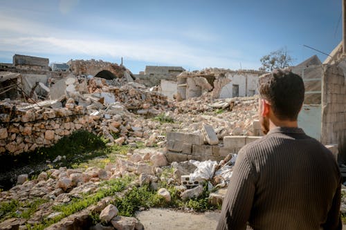 Back View Shot a Man Looking at the Broken Houses