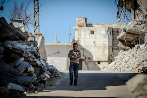 Free A Young Boy Walking on the Street Between Demolished Houses Stock Photo