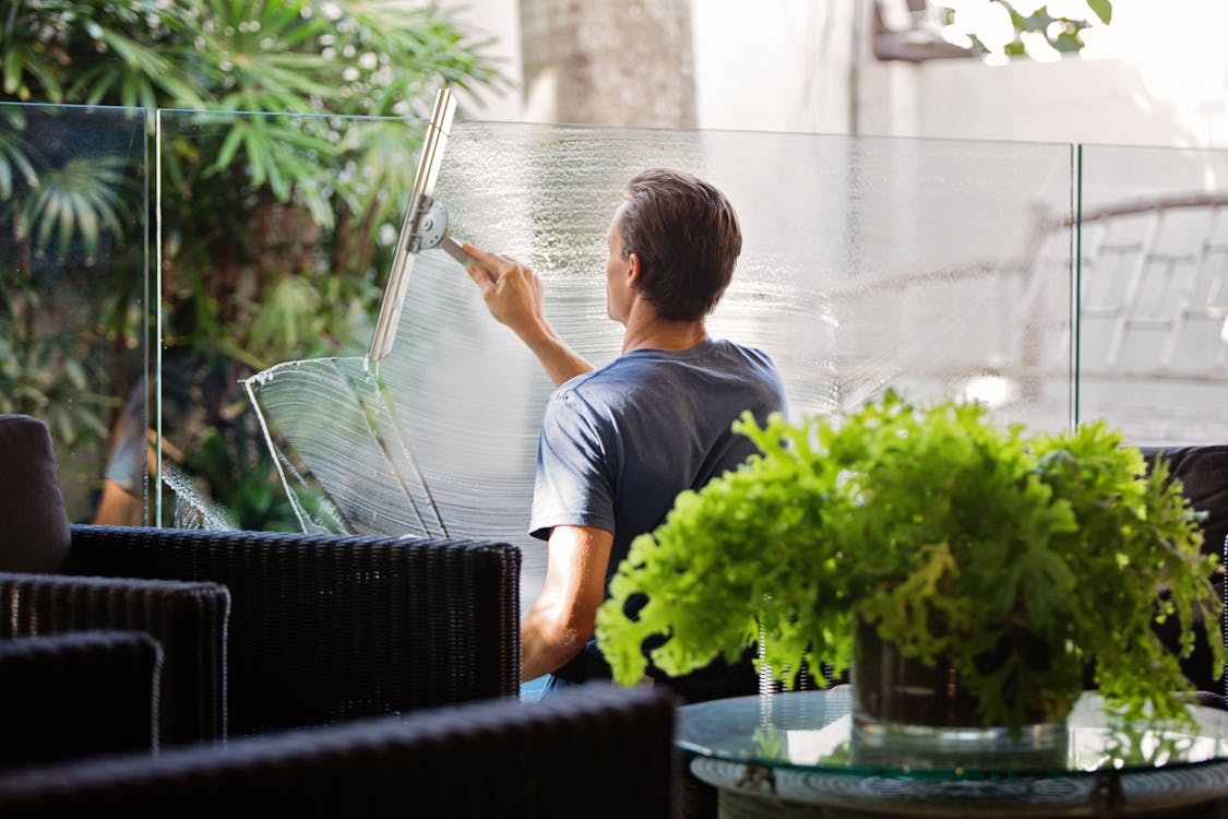 Free Man in Gray Shirt Cleaning Clear Glass Wall Near Sofa Stock Photo
