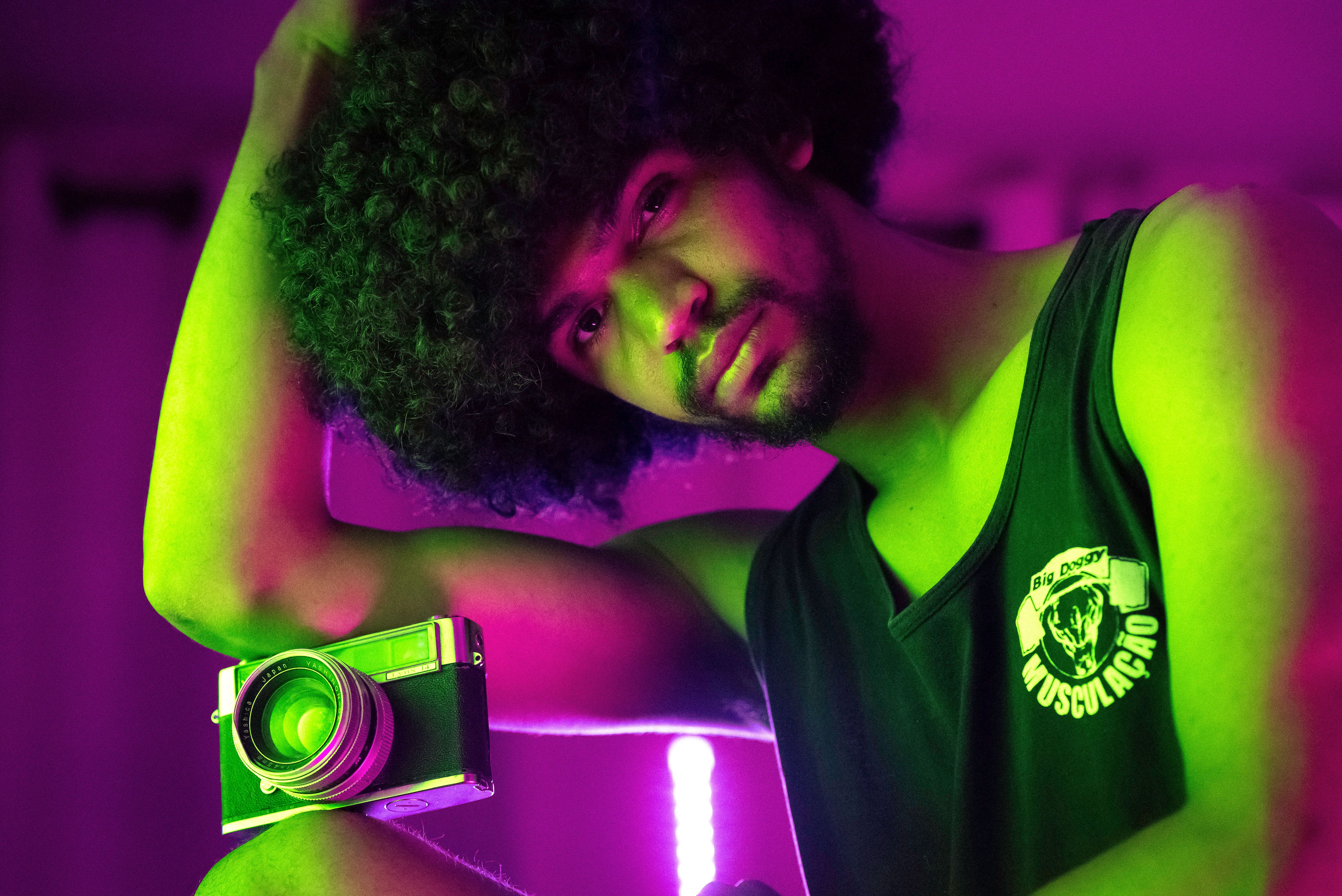 African American male with Afro hairstyle and old fashioned photo camera on knee looking at camera while sitting in room with glowing lamps