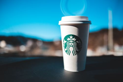 Free Close-up of a coffee cup outdoors, highlighting the brand logo against a scenic background. Stock Photo