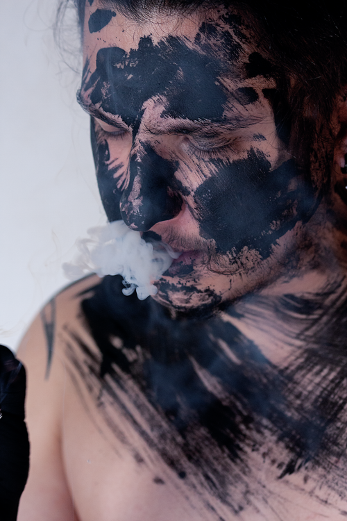 Free Creative photo of a man with ink on face and body, exhaling smoke. Stock Photo
