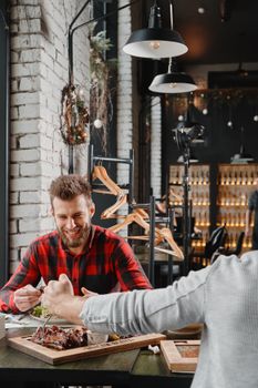 A bearded man enjoys a meal with a friend in a trendy Argentinian restaurant setting.