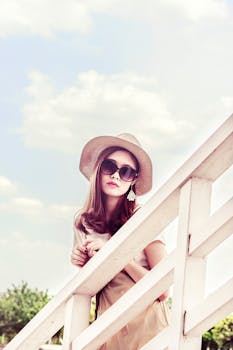 A fashionable woman poses outdoors wearing sunglasses and a straw hat on a sunny summer day.