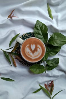 Top view of a cappuccino with latte art surrounded by leaves.