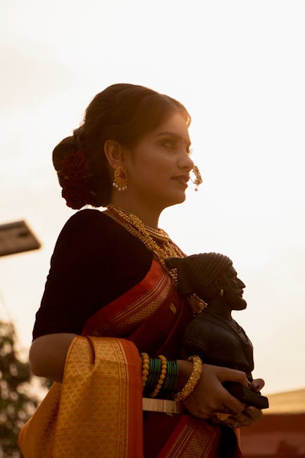 A woman in traditional Indian dress holding a statue during sunset, embodying south Asian culture.