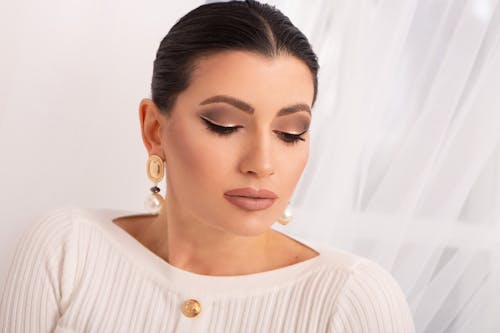 Elegant female with black eyeliner and eyeshadows on face looking down on white background