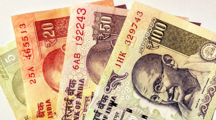 Close-up of Indian rupee banknotes being counted by hand at a currency exchange counter before an Umrah trip