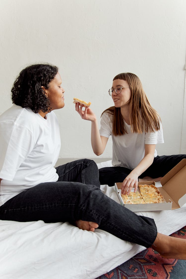 A Couple Eating Pizza On The Bed