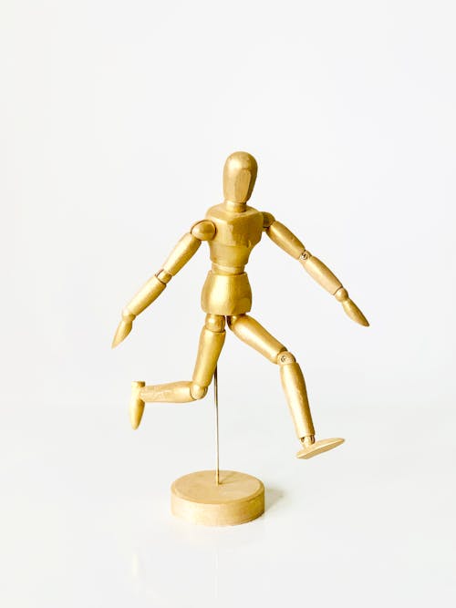 Close-Up Shot of a Gold Wooden Figurine on a White Surface