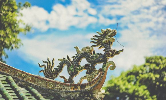 Intricate dragon sculpture decorates a rooftop against a bright blue sky.