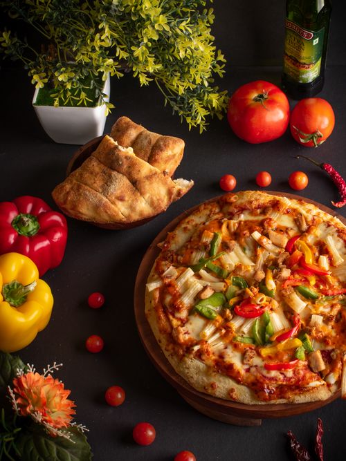 Free Mouthwatering pizza with vibrant peppers and tomatoes surrounded by fresh ingredients. Stock Photo