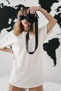 Anonymous female photographer in white t shirt taking picture on photo camera while standing on bed in light room at home