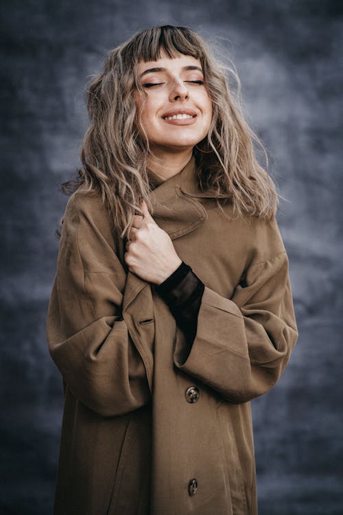 Charming female in coat standing with closed eyes against blurred background