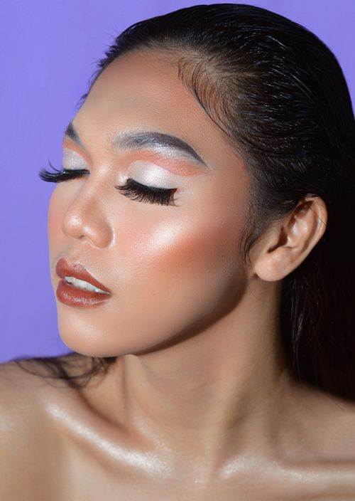 Free Close-up portrait of a woman with creative makeup and eyes closed, set against a purple background. Stock Photo