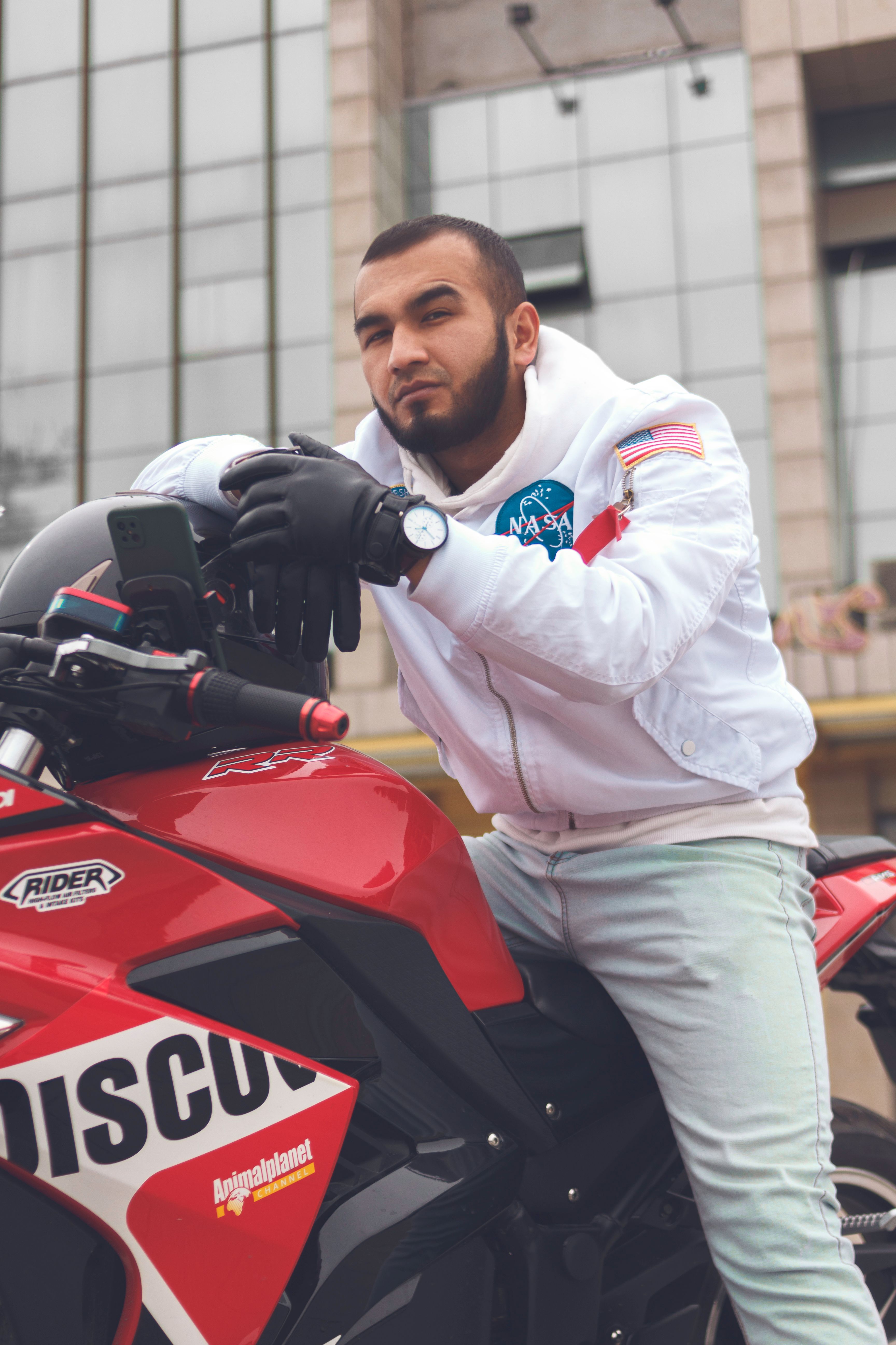 Man in white jacket posing on red motorcycle in urban area. Stylish and adventurous theme.