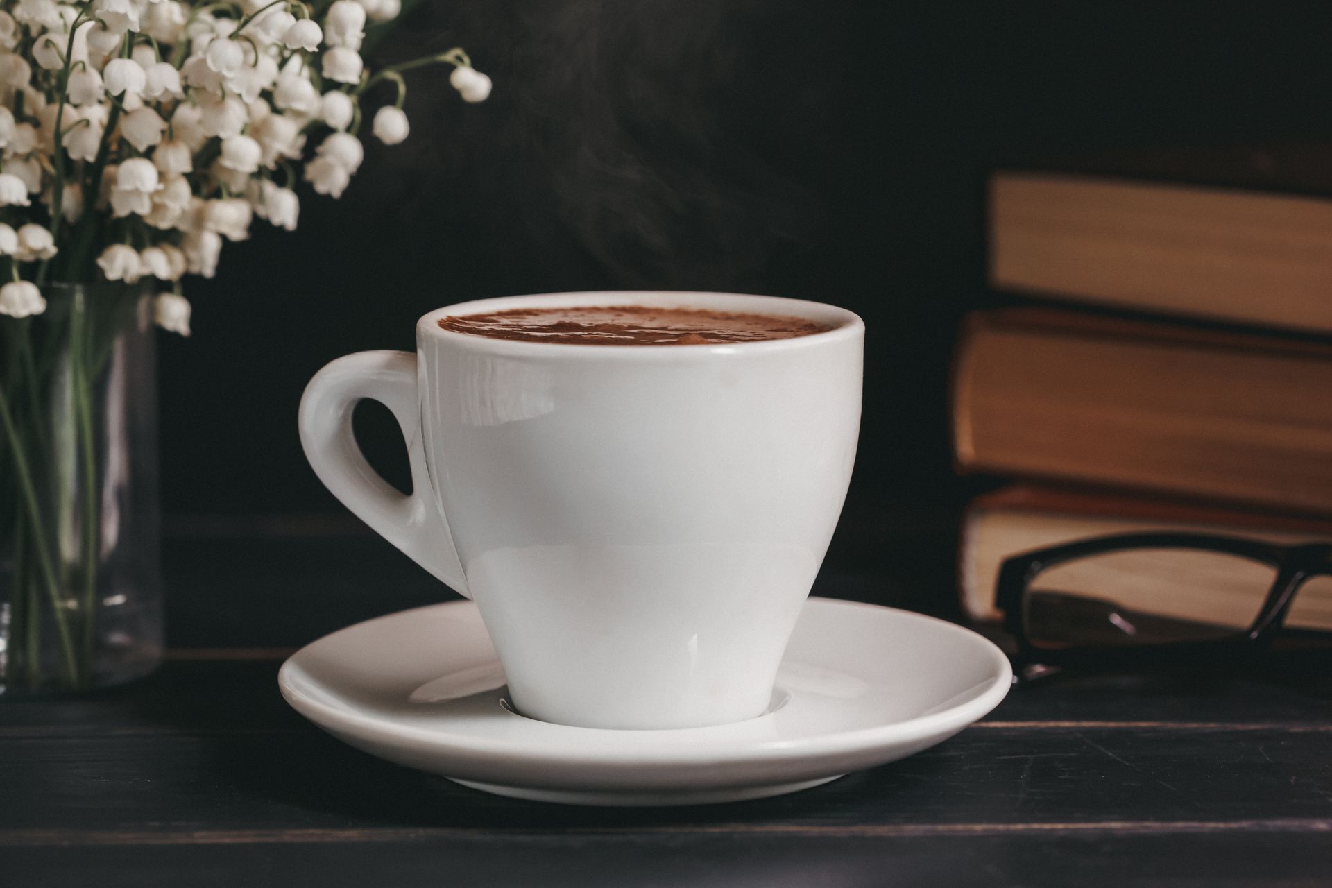 Warm cup of hot chocolate surrounded by books and fresh lily of the valley flowers for a cozy ambiance.