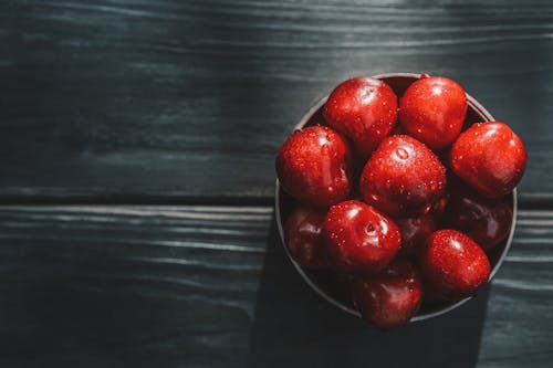 Top view pile of red fresh washed acerola cherries in bowl placed on black wooden table