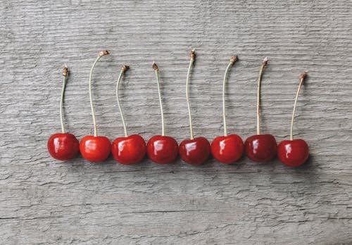 Top view of appetizing red ripe cherries placed on wooden table in row in sunlight