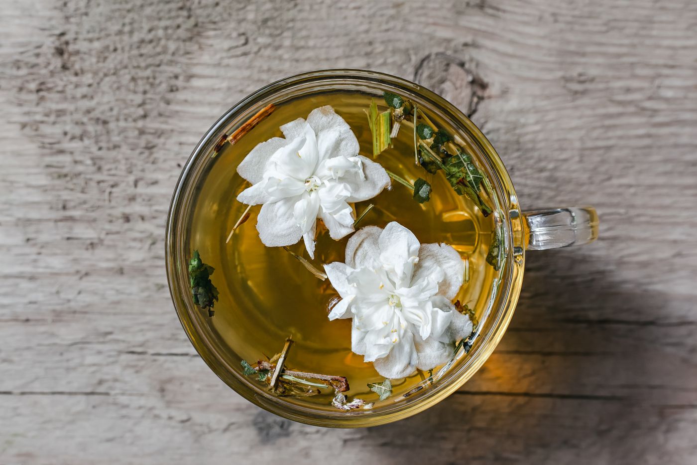 Brewed jasmine tea in a glass cup with fresh jasmine blossoms, showing the pale liquor color