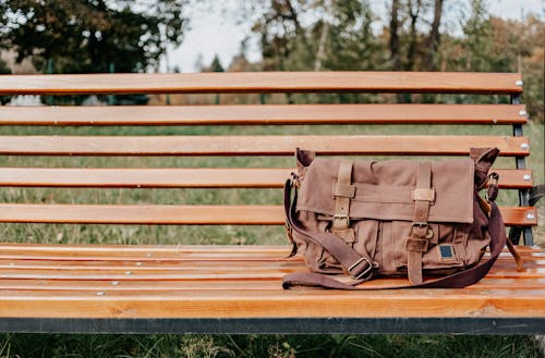 Bag placed on wooden bench in green park