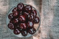 Top view of delicious whole sweet cherries in glass bowl on fabric on sunny day