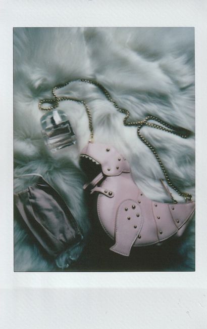 A chic flat lay of a dinosaur-shaped bag, perfume, and face mask on a furry surface.