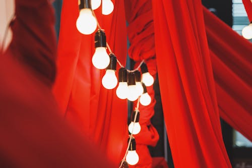 From below of bright garland made of light bulbs and hanging between textile with pleats