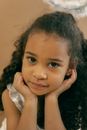 Cute African American girl with curly hair and brown eyes wearing angel nimbus leaning on hand and looking at camera