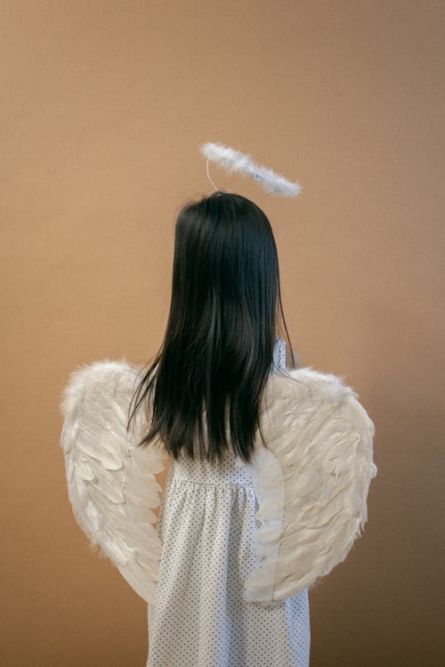 Small girl wearing angel costume standing near beige wall