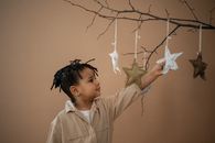 Cute black boy touching soft handmade stars hanging on branch