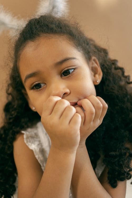 Adorable little African American girl with curly hair and nimbus above head leaning on hand and looking away