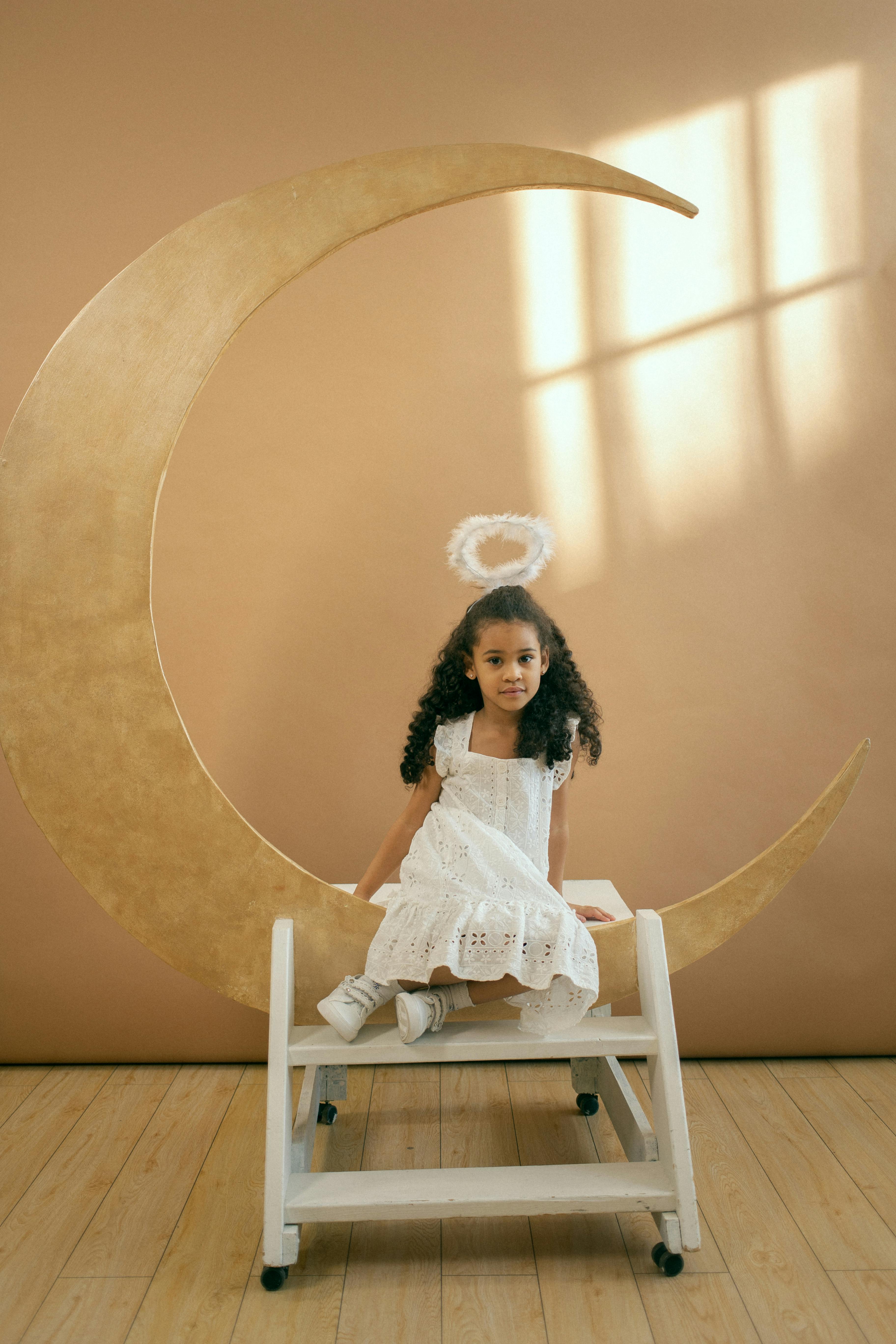 small black girl in angel costume sitting on crescent moon