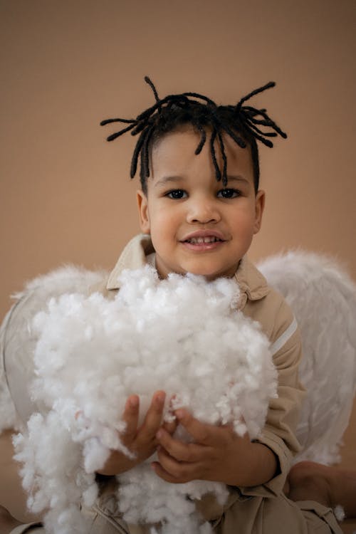 Cheerful black boy in angel costume with cotton in hands