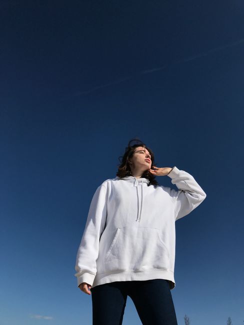 Low angle of peaceful female with closed eyes in casual hoodie and jeans standing against blue sky