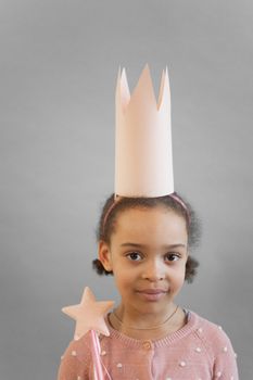 Adorable African American girl with magic wand in hands wearing crown and looking at camera on gray background in studio
