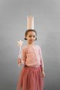 Cheerful African American girl wearing princess crown looking at camera while standing on gray background with magic wand in hand