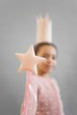 Soft focus of anonymous African American girl in princess crown showing magic wand while standing on gray background in studio